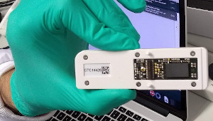 A picture of someone holding a nanopore device, approximately the size of an oversize usb stick with a chip visible.